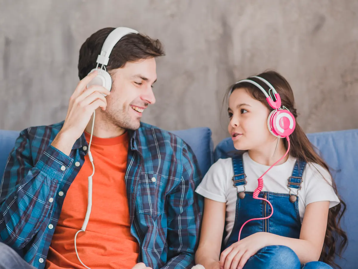 A father and his daughter on the sofa, listening together with headphones on.